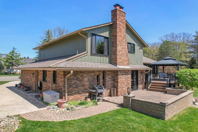 rear view of house with board and batten siding, a chimney, brick siding, a gazebo, and a patio