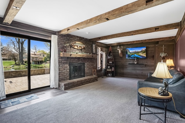living area with wooden walls, carpet, beamed ceiling, and a fireplace