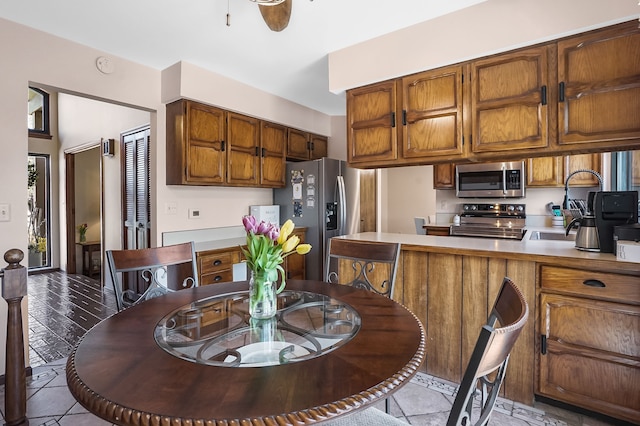 kitchen featuring brown cabinetry, a peninsula, light countertops, a sink, and stainless steel appliances
