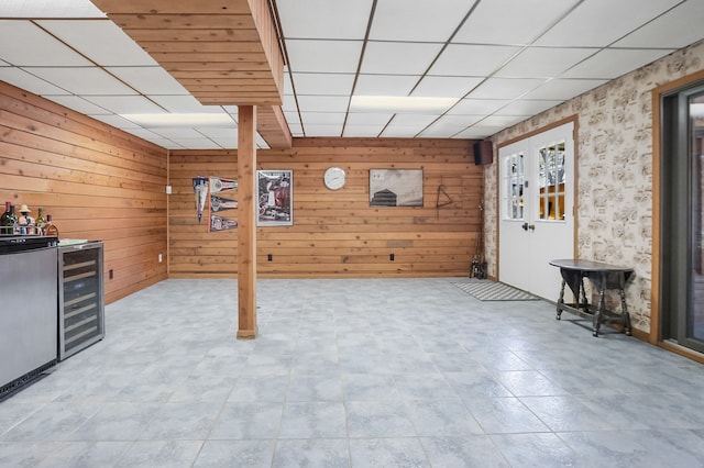 below grade area featuring wooden walls, a drop ceiling, and wine cooler
