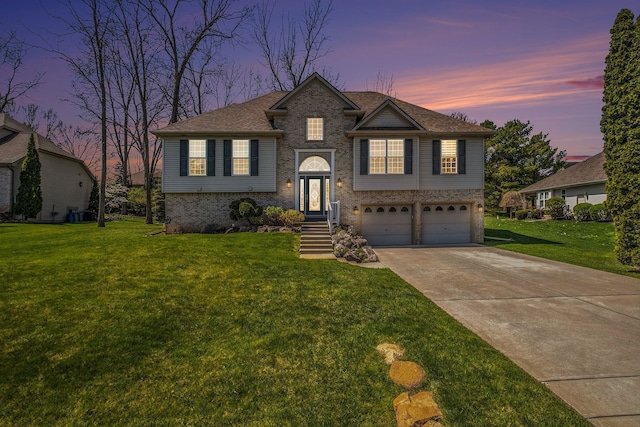 split foyer home featuring a garage, a front lawn, brick siding, a shingled roof, and concrete driveway
