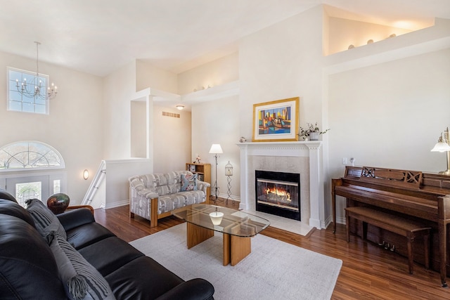 living area with a tiled fireplace, visible vents, wood finished floors, and a notable chandelier