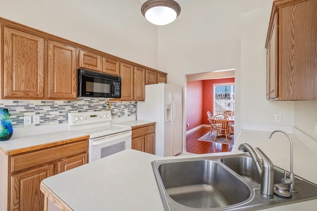 kitchen with white appliances, light countertops, brown cabinets, a sink, and backsplash