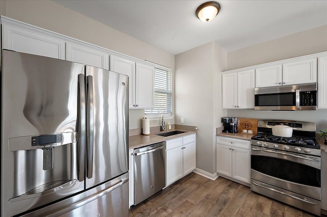kitchen featuring appliances with stainless steel finishes, dark wood finished floors, light countertops, a sink, and white cabinets