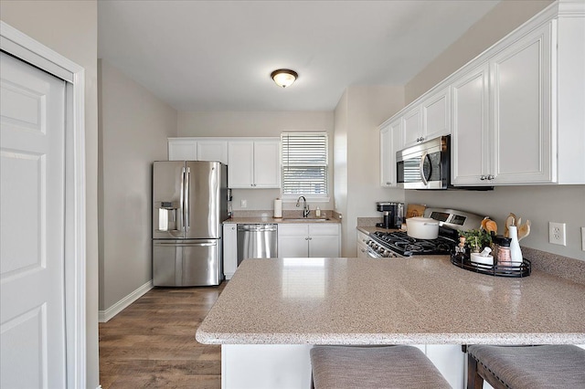 kitchen featuring a peninsula, dark wood-type flooring, white cabinetry, a sink, and stainless steel appliances
