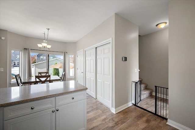 kitchen featuring pendant lighting, wood finished floors, baseboards, a notable chandelier, and white cabinetry