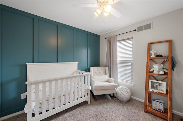 carpeted bedroom featuring baseboards, visible vents, a crib, and ceiling fan