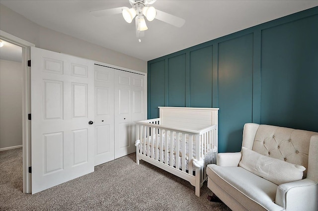 carpeted bedroom featuring a decorative wall, a nursery area, ceiling fan, and a closet