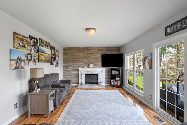 living room featuring visible vents, a brick fireplace, wood finished floors, baseboards, and wooden walls