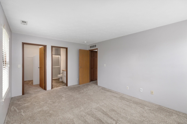 unfurnished bedroom featuring ensuite bathroom, light colored carpet, and visible vents