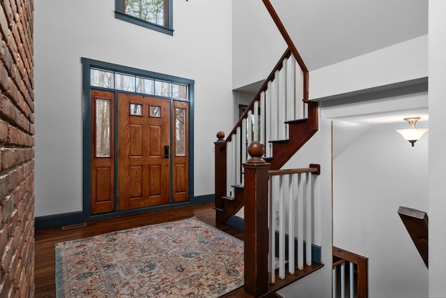 foyer entrance with stairs, baseboards, wood finished floors, and a towering ceiling