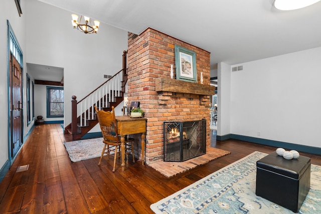 living area featuring visible vents, a fireplace, stairway, an inviting chandelier, and hardwood / wood-style floors
