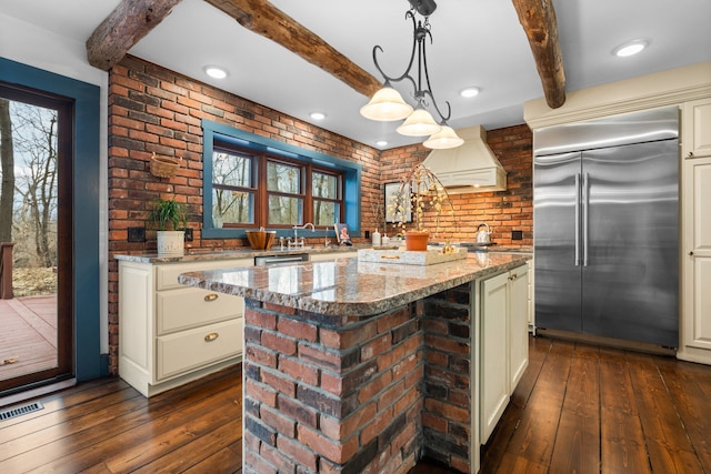 kitchen featuring light stone countertops, beamed ceiling, dark wood-style floors, premium range hood, and built in refrigerator