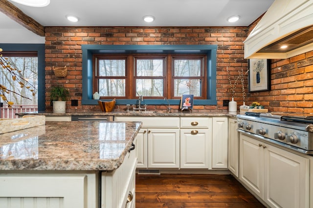 kitchen featuring brick wall, stainless steel gas cooktop, dark wood finished floors, a sink, and custom range hood