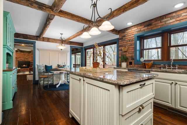 kitchen featuring dark wood-style flooring, a center island, light stone countertops, a sink, and beamed ceiling