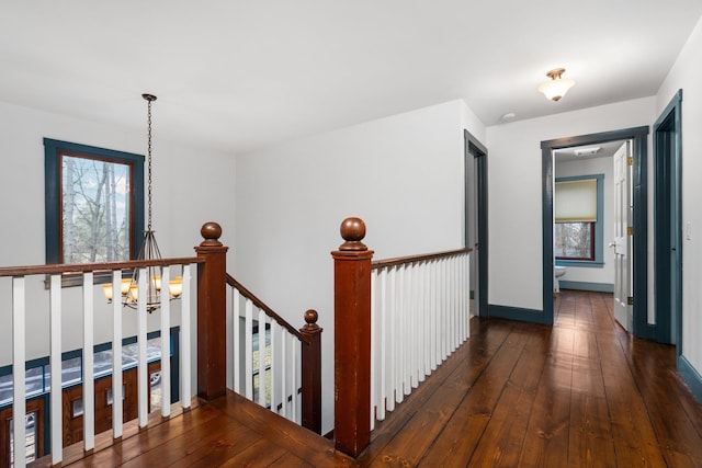 hall with baseboards, a chandelier, hardwood / wood-style floors, and an upstairs landing