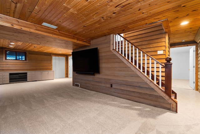 unfurnished living room featuring carpet floors, wood walls, stairs, and visible vents