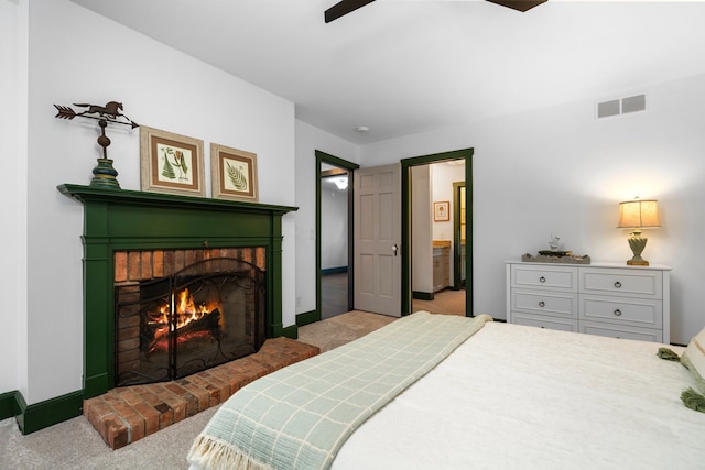 carpeted bedroom with visible vents, a brick fireplace, baseboards, ceiling fan, and connected bathroom