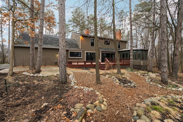 back of property featuring roof with shingles, a chimney, a sunroom, and a deck