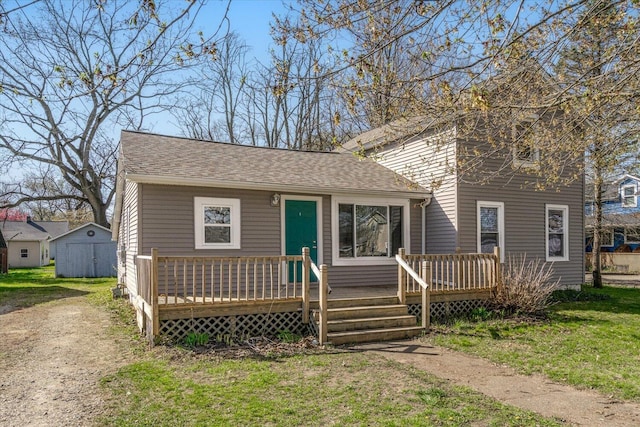view of front of house with an outdoor structure, a front lawn, a wooden deck, a shed, and a shingled roof