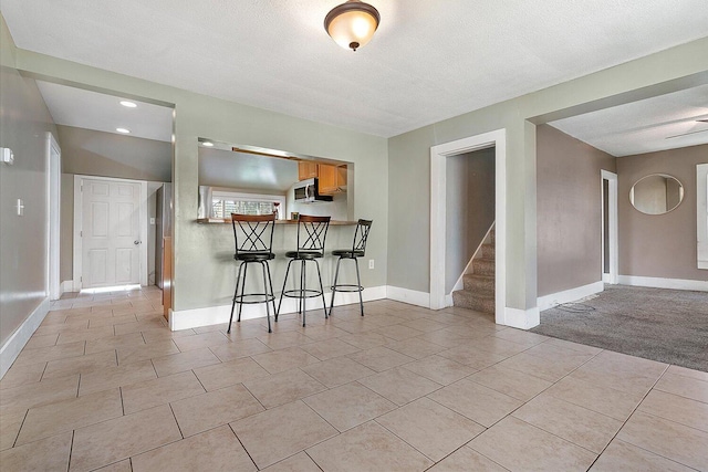 kitchen featuring baseboards, a kitchen breakfast bar, stainless steel microwave, and light tile patterned floors