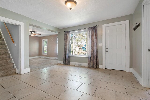 foyer with a ceiling fan, a textured ceiling, stairway, light tile patterned floors, and baseboards
