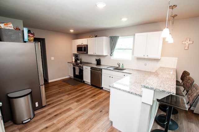kitchen with white cabinets, appliances with stainless steel finishes, a breakfast bar, a sink, and a peninsula