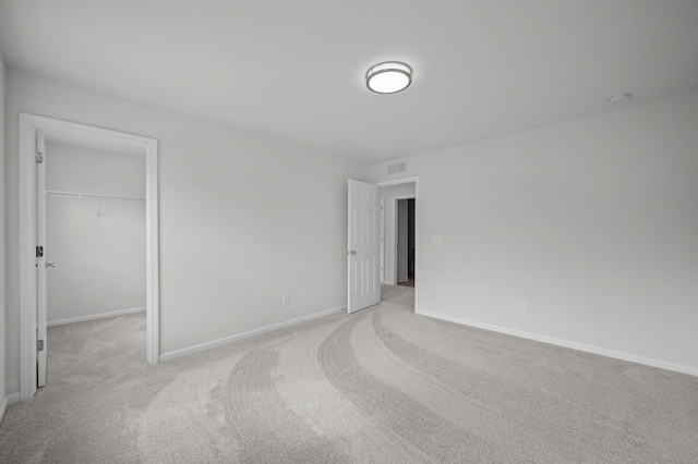 unfurnished bedroom featuring a walk in closet, baseboards, carpet, and visible vents