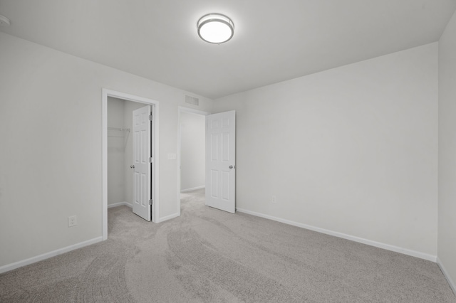 unfurnished bedroom featuring visible vents, a closet, baseboards, a walk in closet, and carpet flooring