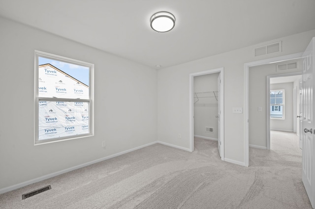 unfurnished bedroom featuring baseboards, visible vents, light carpet, and a spacious closet