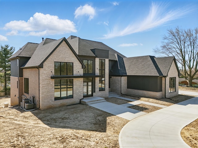 view of front of property featuring a shingled roof, stone siding, french doors, and central AC