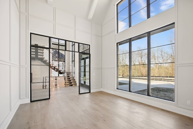 3281 Chickering Ln, Bloomfield Hills, MI 48302 - unfurnished room with a decorative wall, light wood-style flooring, stairway, beam ceiling, and high vaulted ceiling