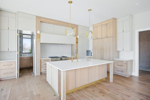 kitchen featuring a sink, light wood finished floors, a center island with sink, light countertops, and recessed lighting