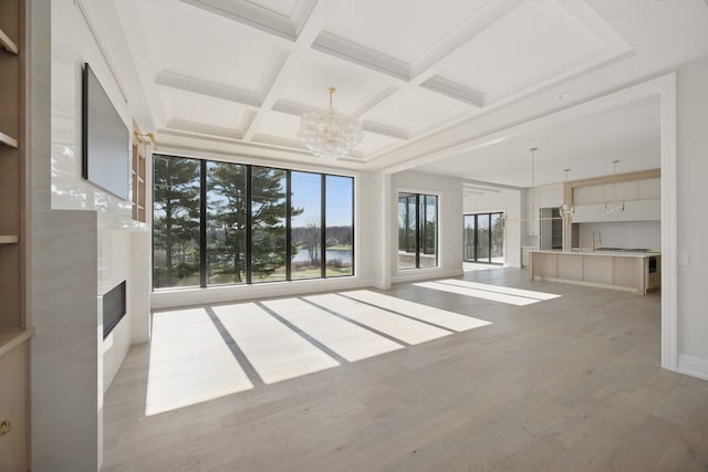 unfurnished living room featuring a chandelier, a water view, light wood-style flooring, beamed ceiling, and coffered ceiling
