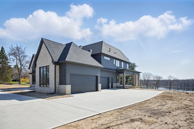 view of property exterior with roof with shingles, a garage, stone siding, concrete driveway, and a water view