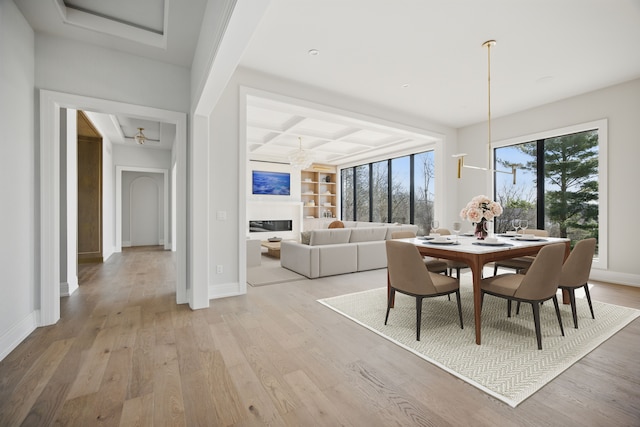 dining room featuring light wood-type flooring, baseboards, a glass covered fireplace, and beamed ceiling