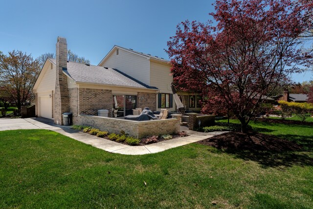 back of house with driveway, a chimney, a lawn, brick siding, and an attached garage
