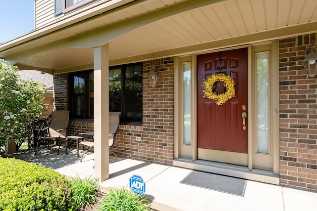 view of exterior entry featuring brick siding and covered porch
