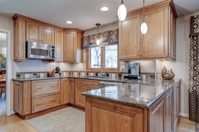 kitchen with a sink, dark stone countertops, light wood finished floors, and stainless steel appliances