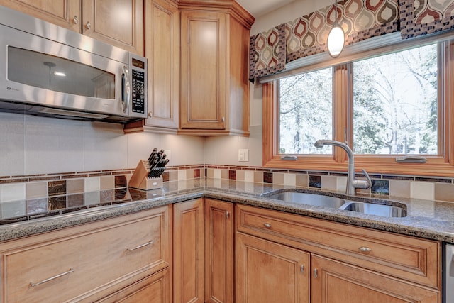 kitchen with stone countertops, a sink, stainless steel microwave, and backsplash