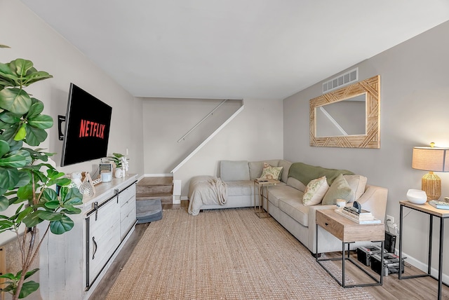 living room with visible vents, light wood finished floors, baseboards, and stairway