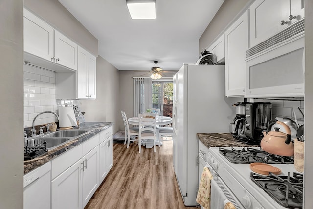 kitchen featuring a sink, light wood finished floors, white appliances, white cabinetry, and backsplash