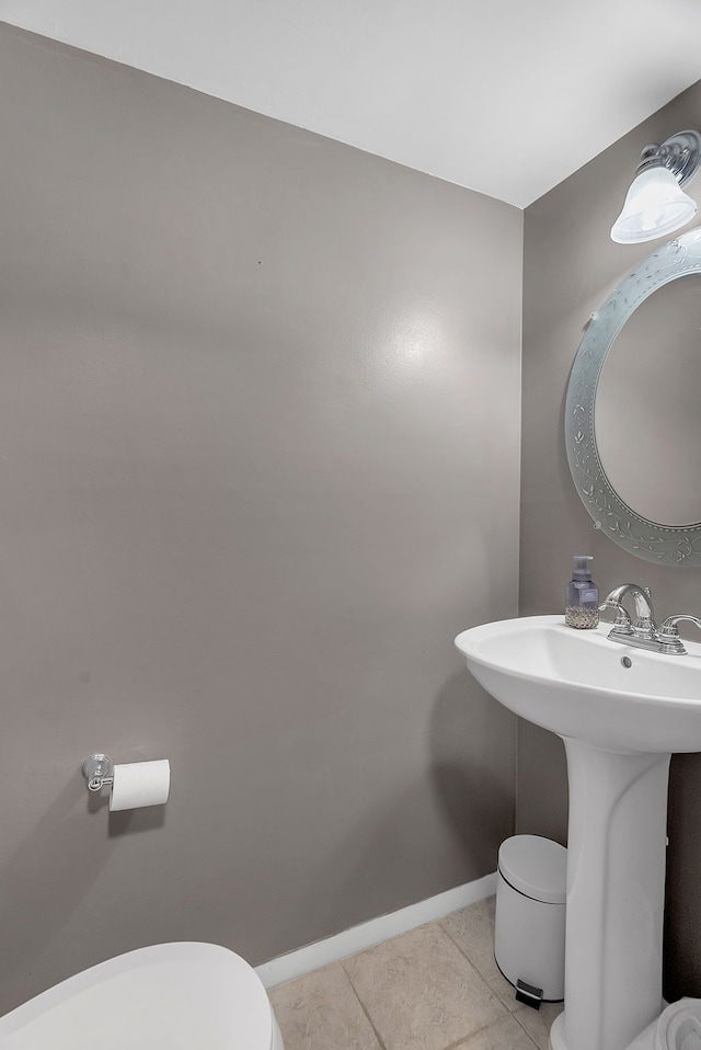 bathroom featuring baseboards, a sink, tile patterned floors, and toilet