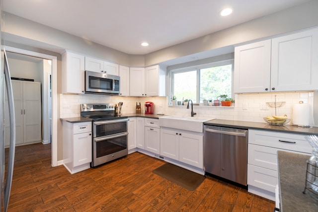 kitchen featuring dark wood-style flooring, dark countertops, white cabinetry, a sink, and appliances with stainless steel finishes