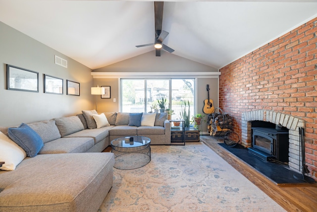 living area with visible vents, a wood stove, wood finished floors, ceiling fan, and lofted ceiling with beams