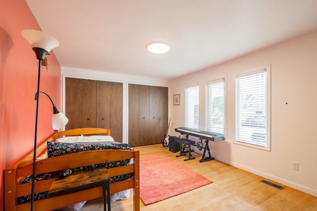 bedroom featuring multiple closets, visible vents, baseboards, and light wood-style floors