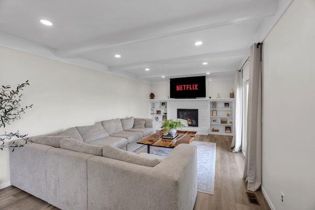living area featuring beam ceiling, a fireplace, recessed lighting, wood finished floors, and visible vents