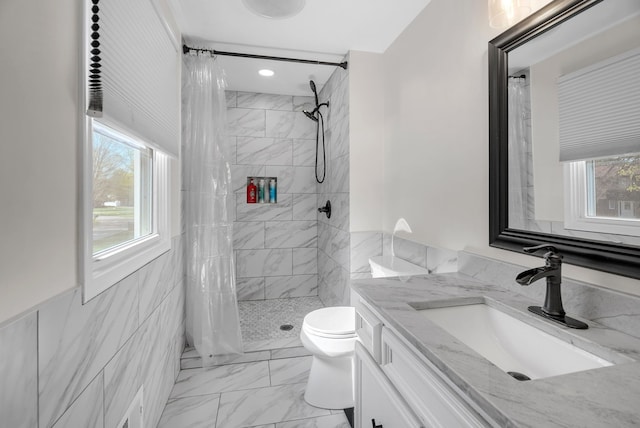 bathroom with tile walls, a tile shower, vanity, toilet, and marble finish floor