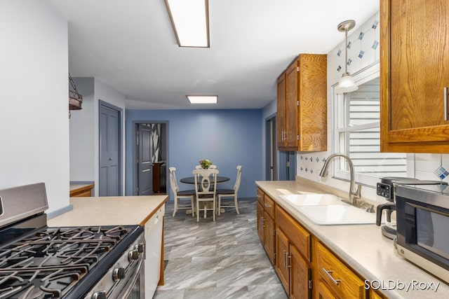 kitchen with light countertops, appliances with stainless steel finishes, brown cabinetry, and a sink