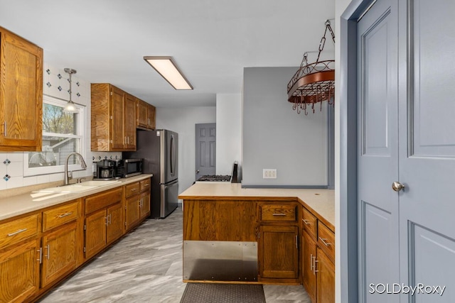 kitchen with a peninsula, light countertops, brown cabinets, a sink, and appliances with stainless steel finishes
